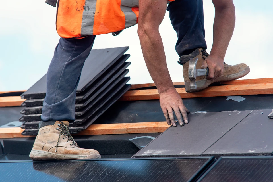Ouvrier en équipement de sécurité installant de l'isolation thermique entre chevrons de toiture dans combles en construction